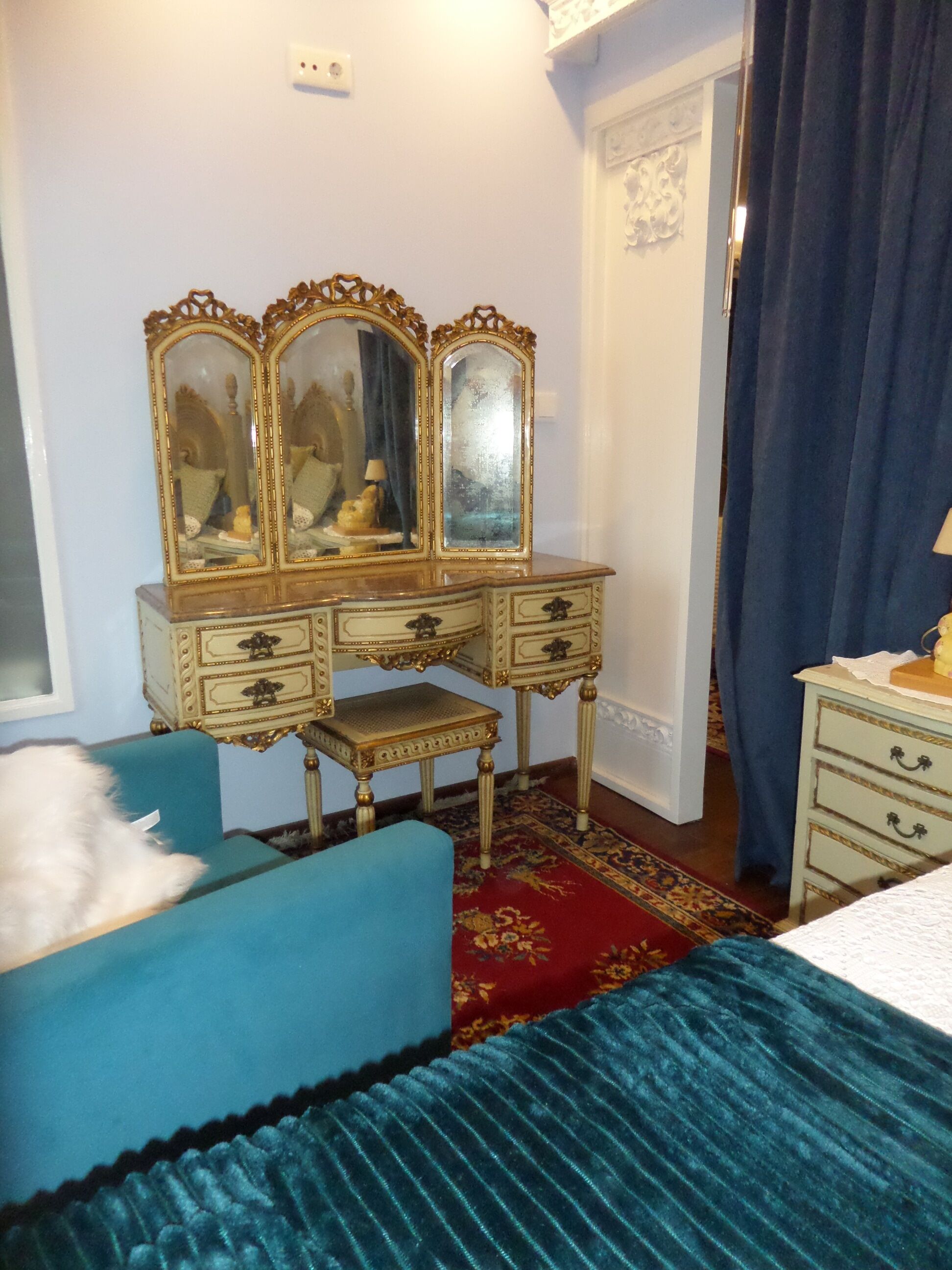 A bedroom with a blue bed, a wooden dresser with a mirror, a small stool, and a blue chair.