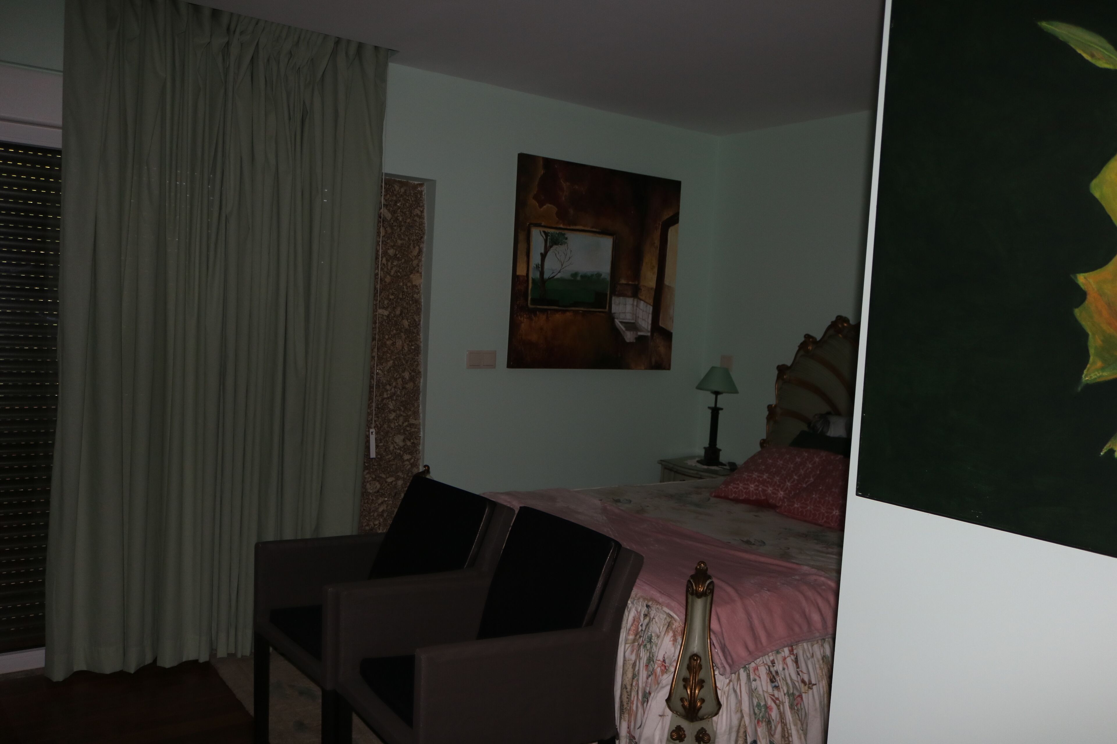 Une chambre à coucher avec un lit, une chaise, un tableau et une fenêtre avec des rideaux.