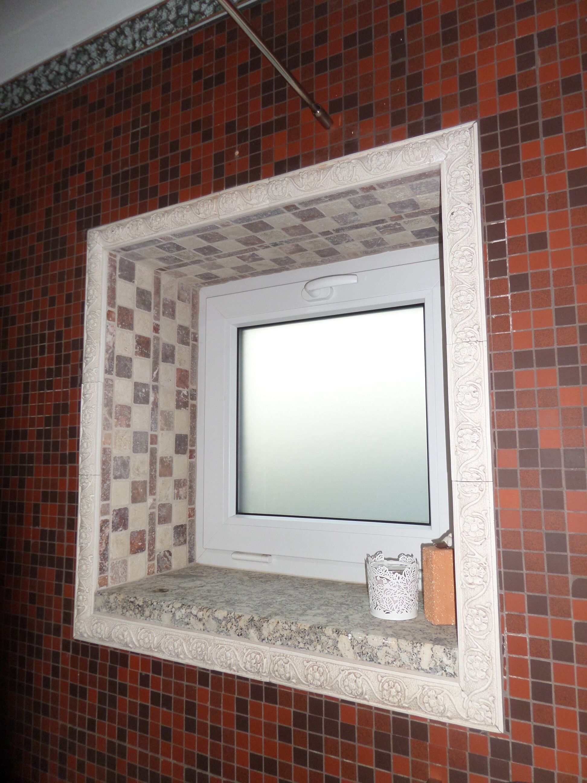 Une salle de bain avec un mur carrelé, un miroir à cadre blanc et une petite étagère sur laquelle est posé un objet décoratif.