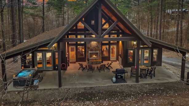 A cabin with a stone fireplace, outdoor seating, and a hot tub. - NEW! Prime Cabin Chateau, Hot Tub-Firepit-Sleeps 6 (Broken Bow)