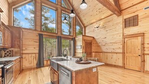 A wooden cabin interior with a kitchen, large windows, and a central island. - NEW! Prime Cabin Chateau, Hot Tub-Firepit-Sleeps 6 (Broken Bow)