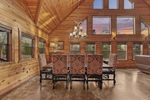 A wooden interior with a dining area, large windows, and a chandelier. - NEW! Prime Cabin, Hot Tub-Firepit-Safari, Sleeps 8 (Broken Bow)
