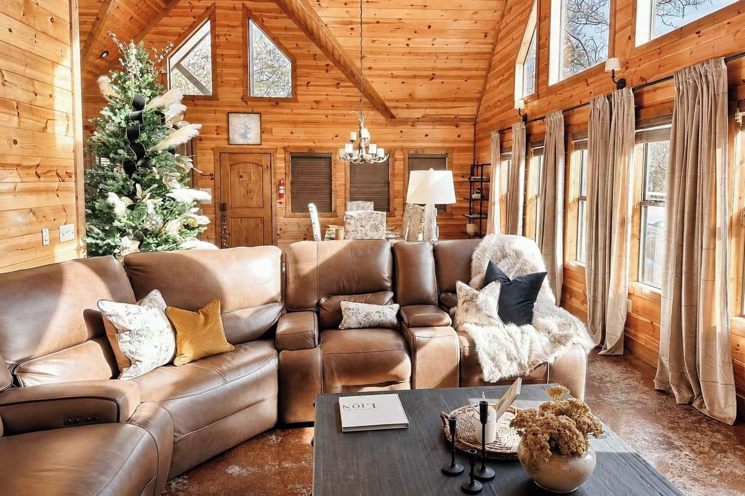 L’intérieur chaleureux d’un chalet en bois, avec un canapé en cuir, un sapin de Noël et une cheminée.