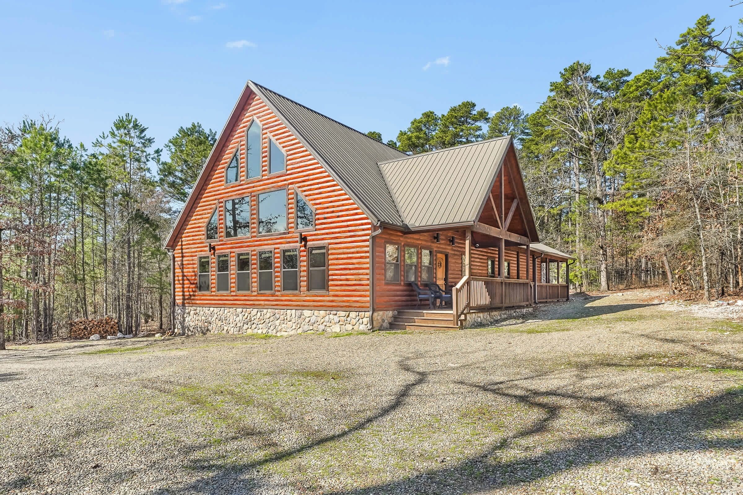 A log cabin with a stone foundation, large windows, and a porch.