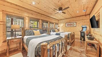 A wooden cabin room with two beds, a ceiling fan, a television, and a fireplace.