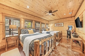 A wooden cabin room with two beds, a ceiling fan, a television, and a fireplace. - As Seen on TV! Safari Views + Hot Tub + Firepit (Broken Bow)