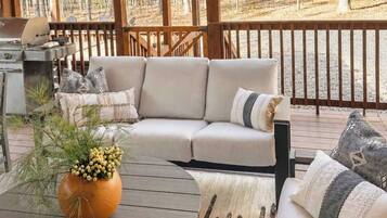 A deck with a sofa, a grill, and a potted plant.