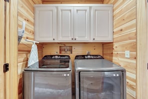 A laundry room with two stainless steel washers, wooden walls, and white cabinets above. - As Seen on TV! Safari Views + Hot Tub + Firepit (Broken Bow)