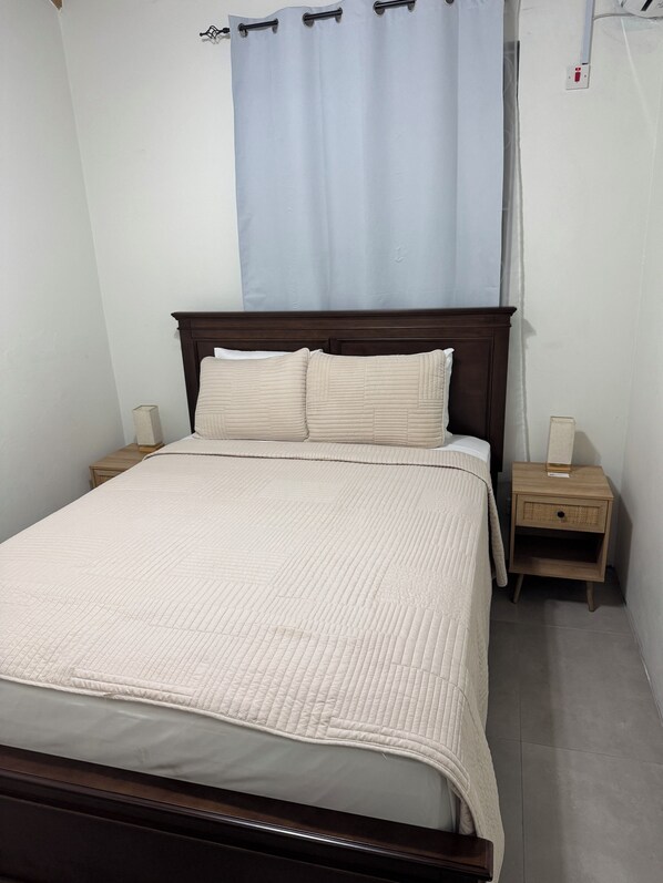 Une chambre à coucher avec un lit, une tête de lit en bois, deux tables de chevet, une commode et un rideau bleu.