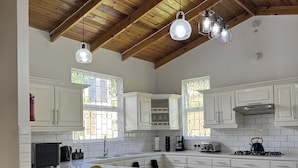 Una cocina moderna con armarios blancos, una isla grande con taburetes, iluminación colgante y techo de madera.