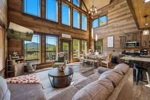 A spacious cabin interior with a large dining area, a kitchen with modern appliances, and a cozy seating area with a view of the outdoors.