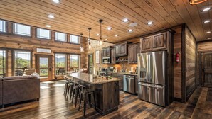 Une cuisine spacieuse avec un plancher en bois, un grand îlot central doté de tabourets, des appareils électroménagers en acier inoxydable et une vue dégagée grâce à de grandes fenêtres.
