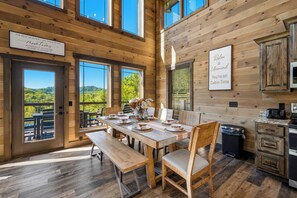 A cabin interior with a dining table set for four, wooden walls, and a view of the outdoors.