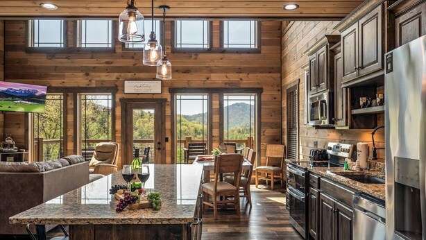 Une cuisine spacieuse dotée de meubles en bois, d’un îlot en granit et d’une grande fenêtre donnant sur un paysage montagneux.
