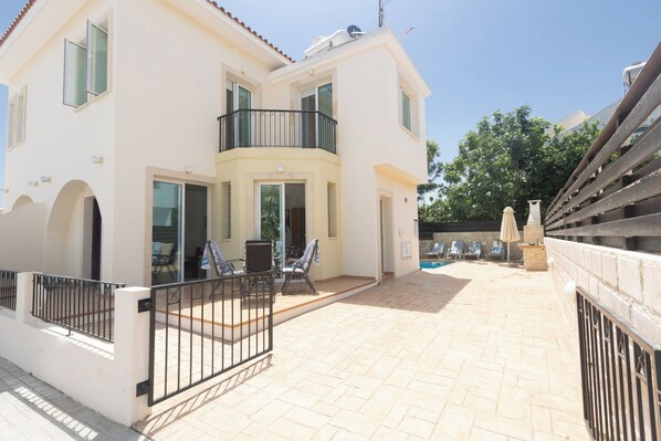 Un bâtiment à deux étages doté d’un balcon, d’un espace extérieur aménagé pour s’asseoir et d’une piscine en arrière-plan.