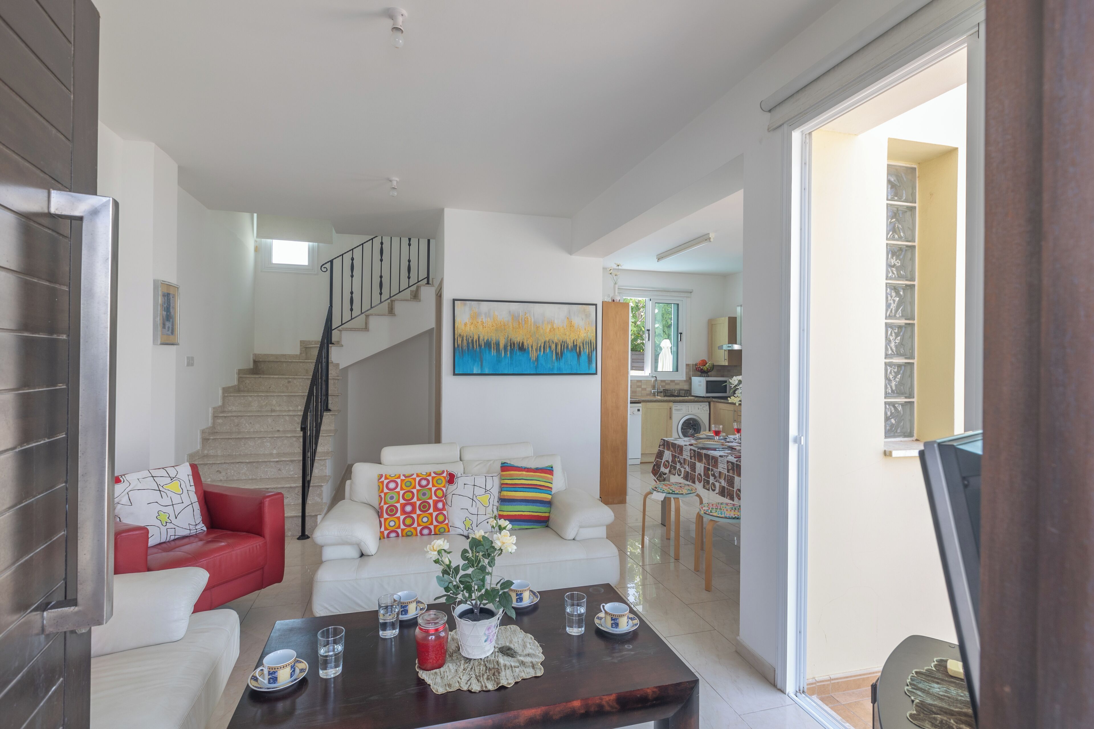 A modern living room with a staircase, a dining area, and a kitchen in the background.
