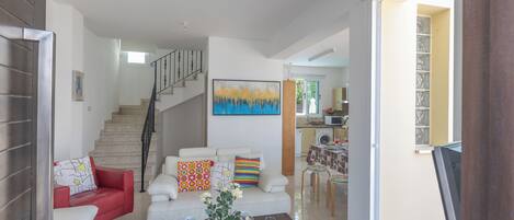 A modern living room with a staircase, a dining area, and a kitchen in the background.