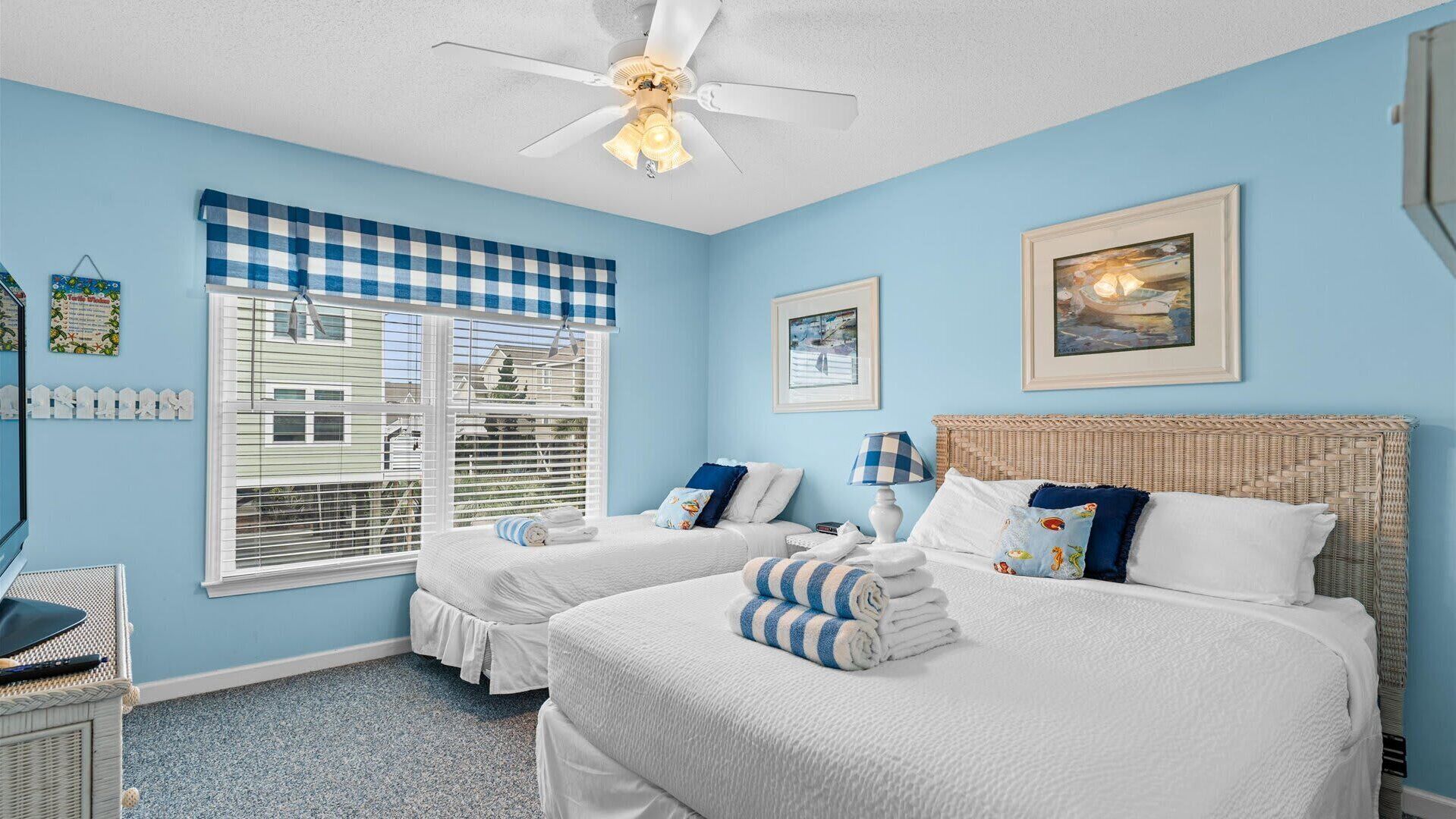 A bedroom with two beds, a ceiling fan, and a window with blinds.