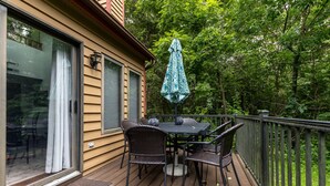 A wooden deck with a table and chairs, an umbrella, and a glass door leading to a room. - Unwind at Star Gazer`s Getaway (Galena)