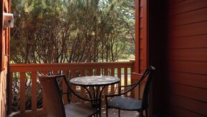 A wooden deck with a round table and two chairs, overlooking a dense forest. - The Old Mill Retreat Sleeps 6! (Bend)