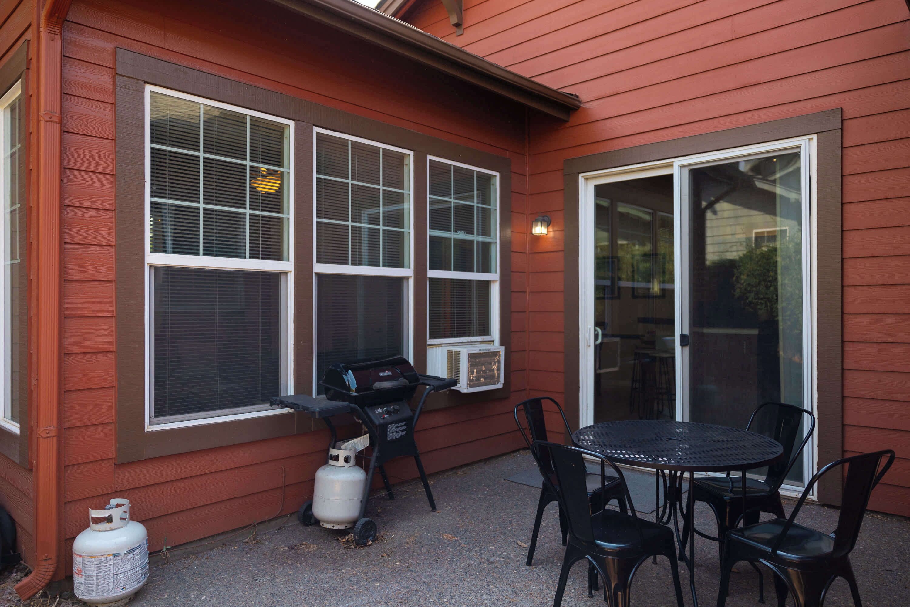Un patio al aire libre con una mesa, sillas, una parrilla y un tanque de propano.