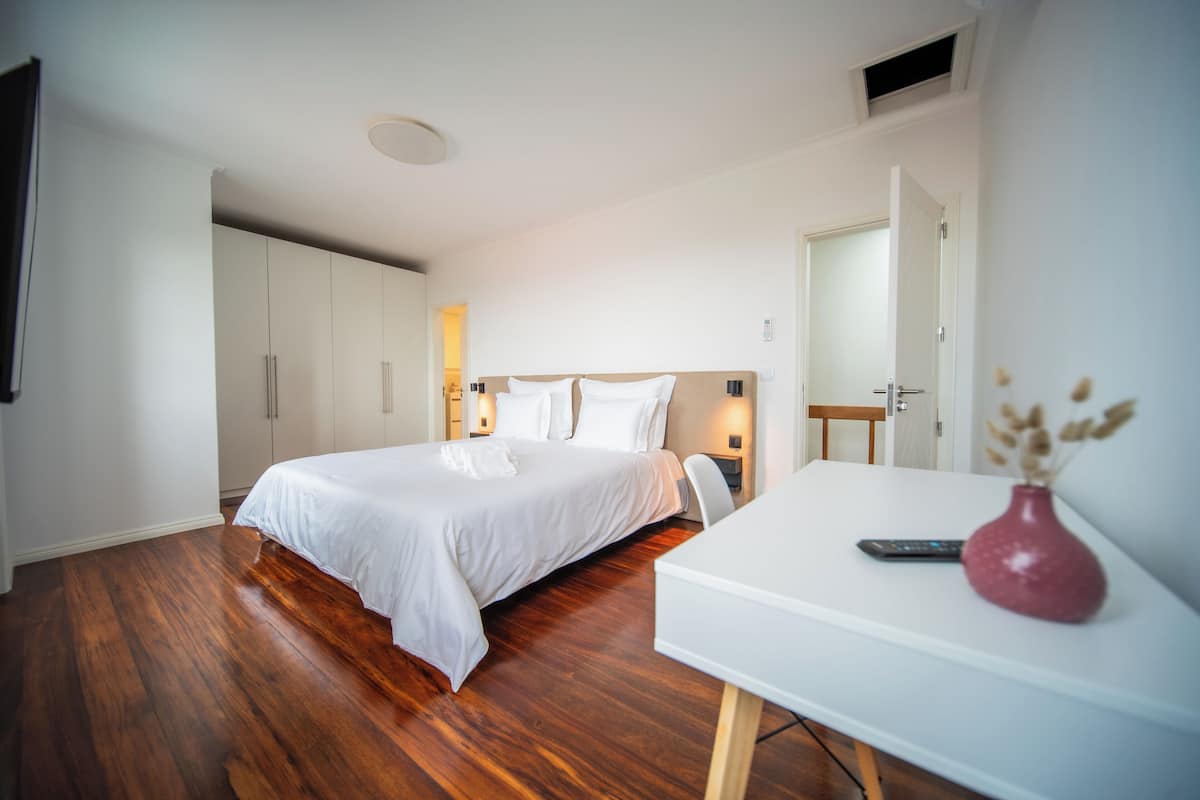 A bedroom with a bed, a desk, a vase, and a remote control.