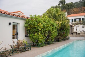 A swimming pool adjacent to a building with a tiled roof, surrounded by lush greenery and a metal fence. - Quinta Da Victória By Venimar (Viana do Castelo)