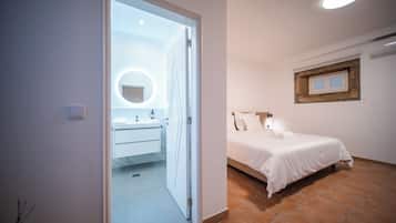 A bedroom with a bed, a bedside table, a nightstand, a window with a wooden frame, and a wall-mounted mirror.