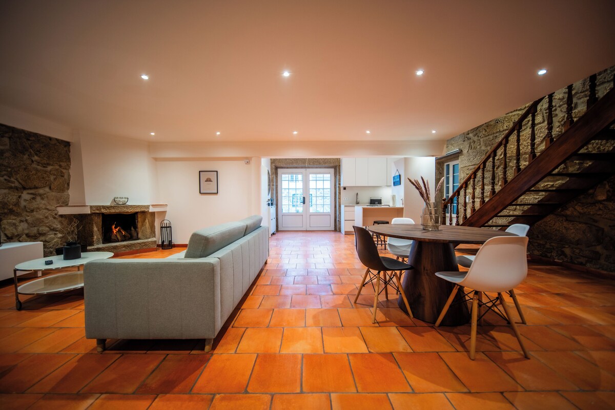 A spacious living area with a fireplace, a dining table with chairs, and a staircase leading to an upper level.