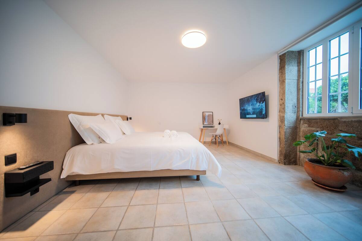 A bedroom with a bed, bedside table, wall-mounted TV, and a potted plant.