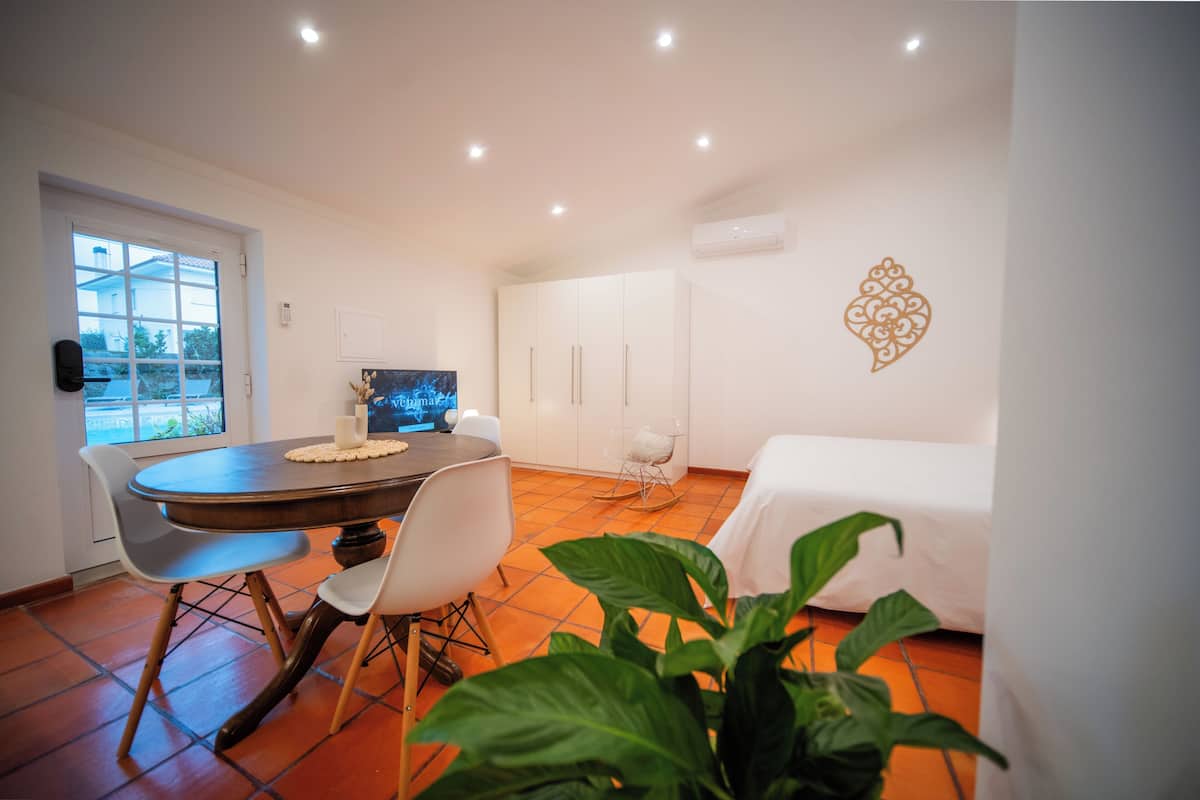 A hotel room with a dining table, chairs, a bed, a TV, and a potted plant.