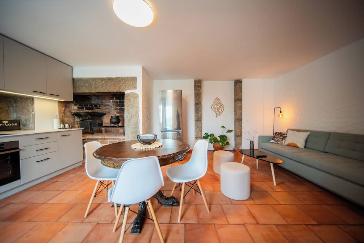 A modern kitchen with a dining area, featuring a round table, white chairs, and a grey sofa.