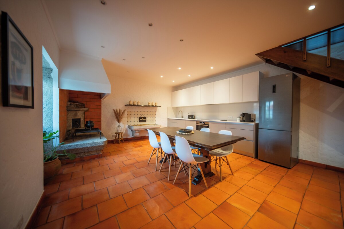 A modern kitchen with a dining area, featuring a brick fireplace, white cabinets, and a large refrigerator.