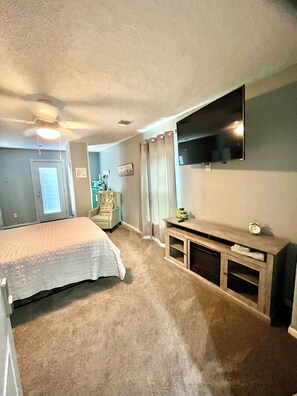 A bedroom with a bed, a TV mounted on the wall, a ceiling fan, and a door. - Let’s get out of LIFE and back to nature (Montgomery)