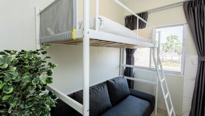 Un lit superposé avec un matelas et des oreillers, un canapé, une plante en pot et une fenêtre avec des rideaux.