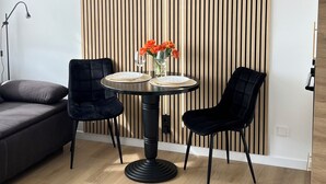 Un salon moderne avec une table ronde, deux chaises noires, un canapé foncé et un mur avec des lambris en bois.