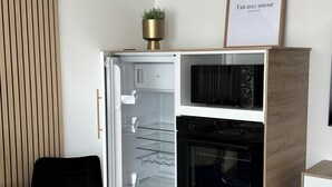 Une cuisine compacte dotée d’un four encastré, d’un petit coin repas avec une chaise noire et d’une plante en pot posée sur le plan de travail.