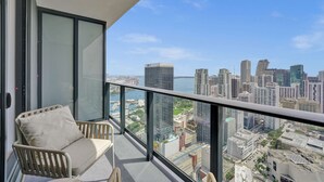 A balcony with a city view, a cushioned chair, and a glass door. - Stylish Studio | Pool Deck | Downtown Miami (Downtown)