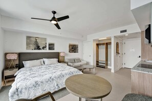 A modern bedroom with a large bed, a bedside table, a nightstand, a round table, and a ceiling fan.