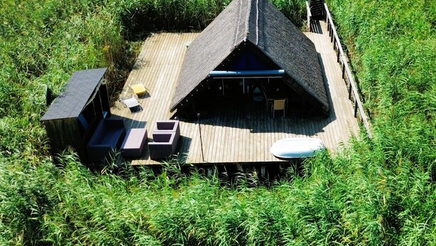 A small, triangular-roofed structure with a wooden deck, surrounded by tall grass. - Mountains&Lakes - Romantika5 Rust (Rust)