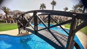 A wooden bridge over a swimming pool with a view of a resort area in the background.