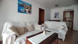 A living room with a white sofa, a wooden coffee table, and a painting of a mountain landscape.