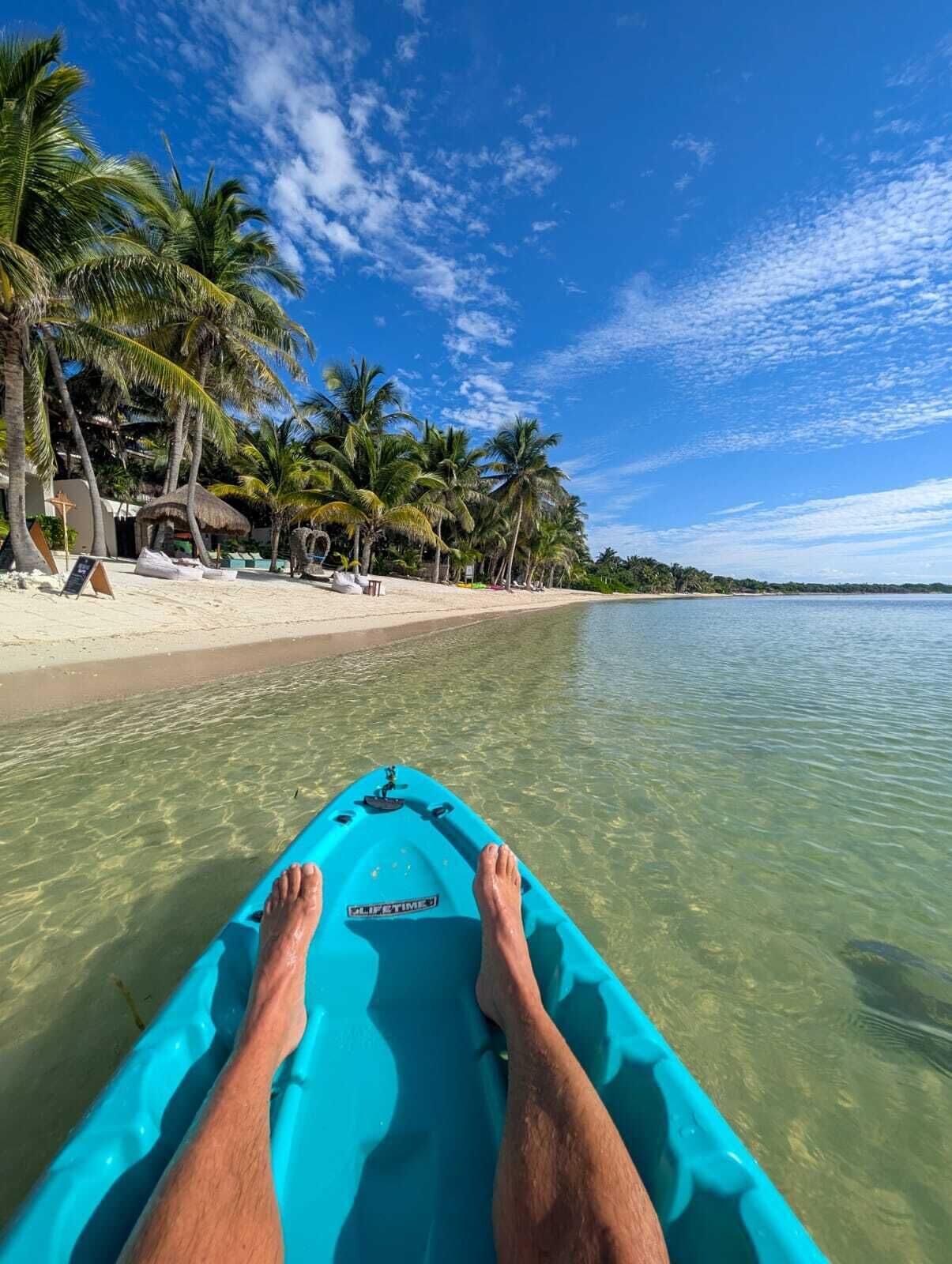 Ein Kajak in Türkis liegt auf einem Strand, im Hintergrund Palmen und ein klarer, blauer Himmel.