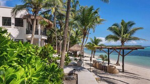 A resort with a beach view, palm trees, and a thatched-roof structure. - La Casa: 3 Bedroom Suite (Tulum)