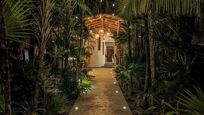 A pathway leading to a building with a thatched roof, surrounded by lush greenery and palm trees. - La Casa: 3 Bedroom Suite (Tulum)