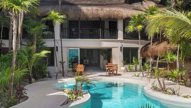A resort with a pool, palm trees, and a thatched-roof building. - La Casa: 3 Bedroom Suite (Tulum)