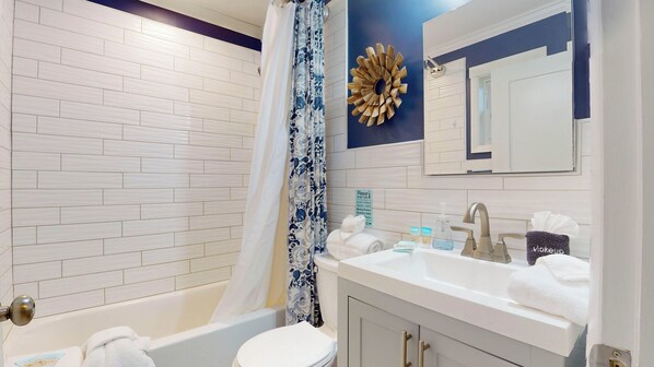 A bathroom with a white bathtub, a toilet, a sink with a mirror, and a shower curtain with a floral pattern.