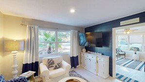 Una sala de estar con televisión, sofá, sillón, aparador y ventana con cortinas.