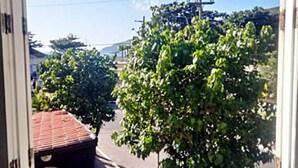 A view through a window of a street with trees, a building with a red roof, and power lines. - Suítes Rolim (Arraial do Cabo)