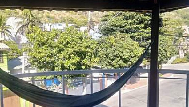 A hammock in a covered outdoor area with a view of a street and greenery. - Suítes Rolim (Arraial do Cabo)